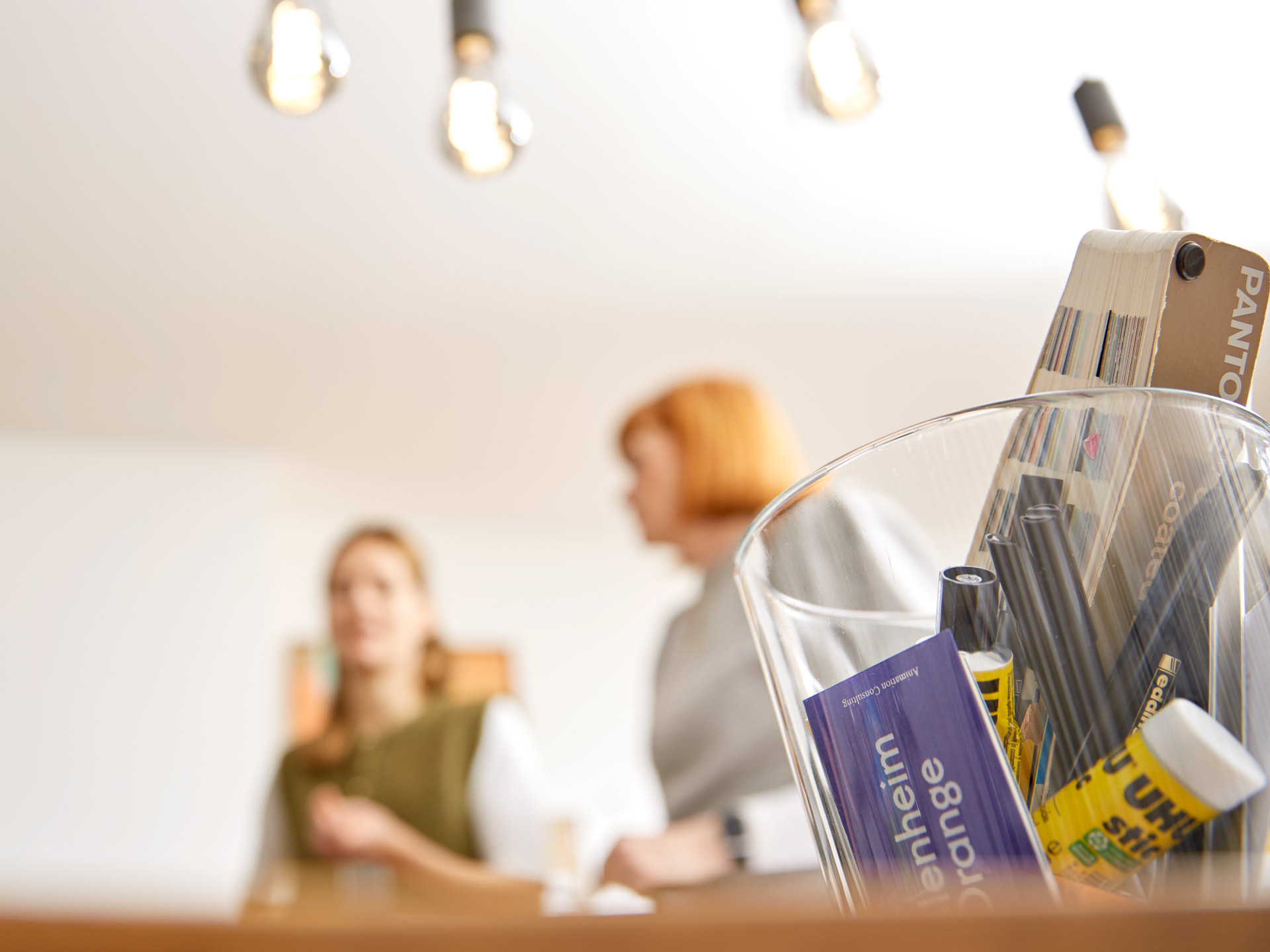 4-workshop-atmosphaere-materialien-tisch Tisch mit Arbeitsmaterialien im Vordergrund, Workshop-Teilnehmerinnen unscharf im Hintergrund